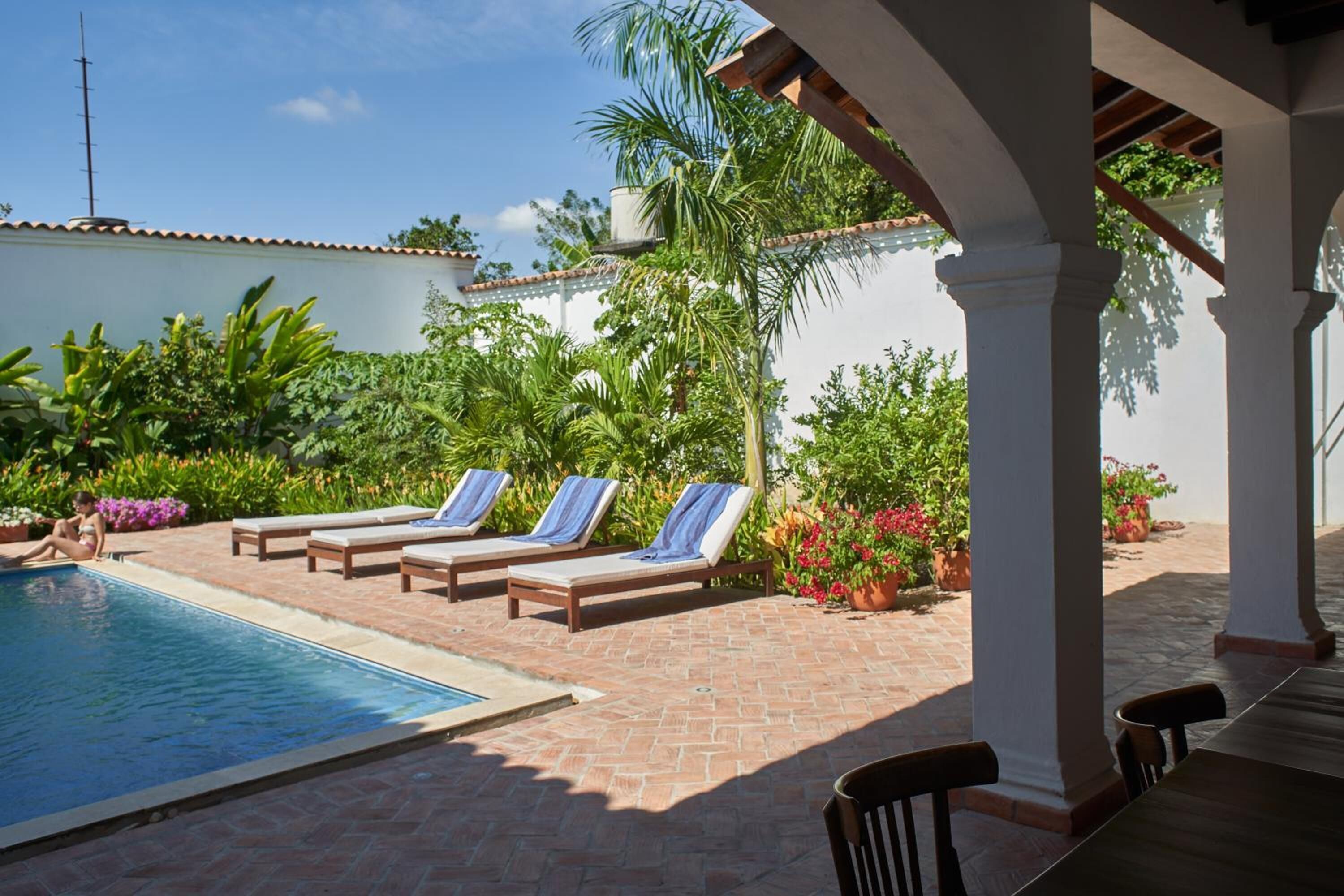 A pool area with lounge chairs, a tiled deck, and surrounding greenery.