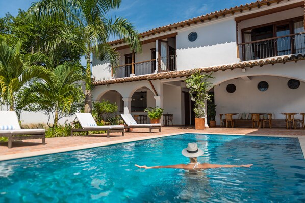 A pool area with lounge chairs and a person swimming.