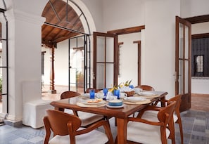 A dining area with a wooden table set for six, surrounded by wooden chairs.