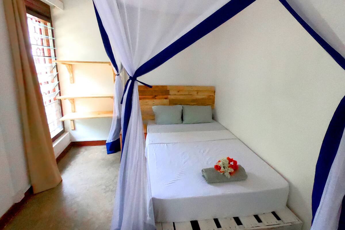 Una cama individual con cabecera de madera, colchón blanco y dosel azul y blanco.