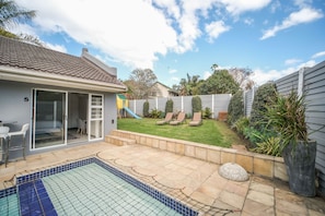 A residential backyard with a swimming pool, a patio area, and a fenced garden. - Lido Living (East London)