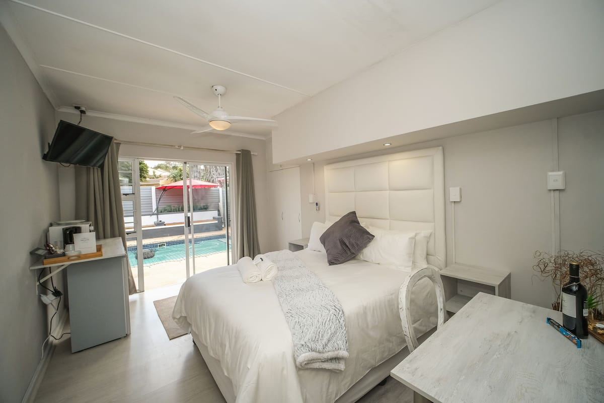 A modern hotel room with a bed, a desk, a TV, and a view of a swimming pool.