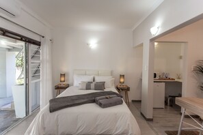 A bedroom with a large bed, bedside tables, a nightstand, a desk, and a view of the outside. - Lido Living (East London)
