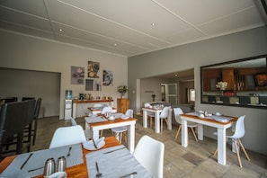 A modern dining area with white tables and chairs, a kitchen in the background, and artwork on the walls. - Lido Living (East London)