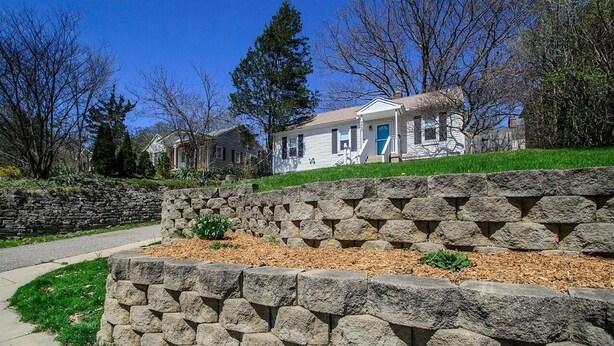 A residential house with a stone retaining wall in front, a clear sky, and a well-maintained lawn. - White House on a Hill (Ann Arbor)