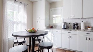 A modern kitchen with white cabinets, a round dining table with four chairs, and a coffee maker on the counter. - White House on a Hill (Ann Arbor)