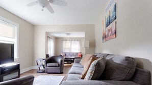 A modern living room with a grey sofa, a black armchair, a TV, and a ceiling fan. - White House on a Hill (Ann Arbor)