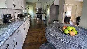 A modern kitchen with stainless steel appliances, a granite countertop, and a dining area with a table set for two. - White House on a Hill (Ann Arbor)
