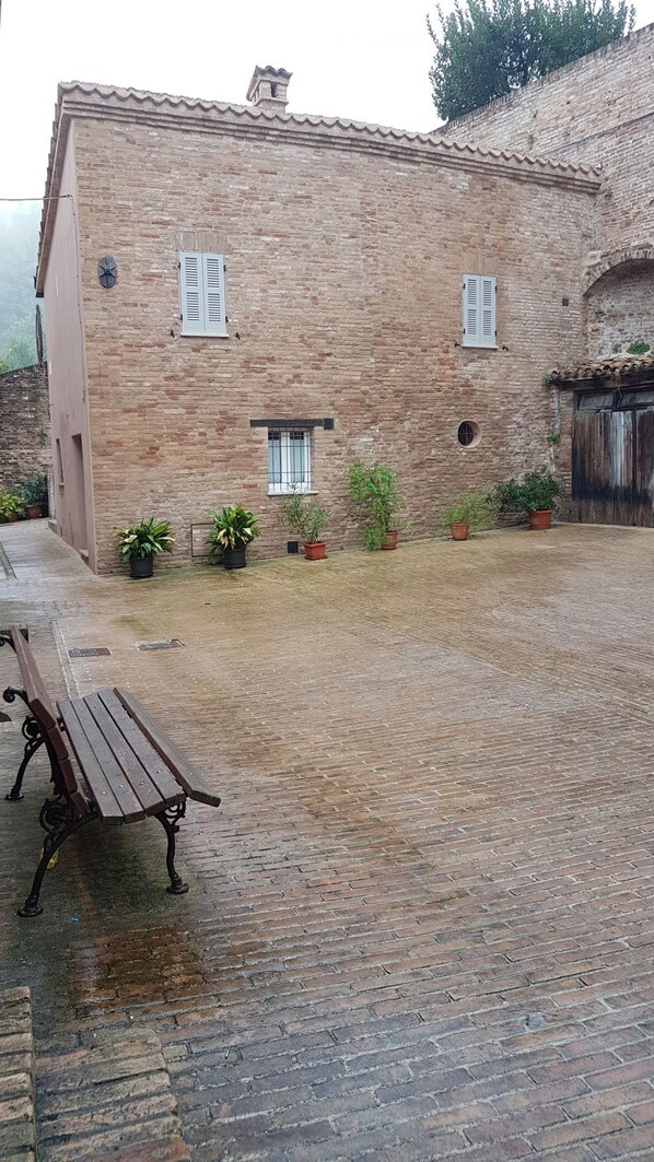 A rustic brick building with a tiled roof, a wooden bench, and potted plants. - Independent Historic Residence Situated on a charming Renaissance Square (Urbino)