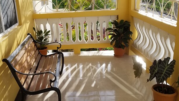 A bench with potted plants on a tiled floor, a white decorative fence, and a yellow wall. - This property is located near Public  and private beaches and restaurants.. (St Ann)