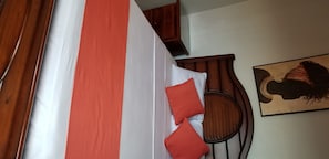 A bed with a striped bedspread, a wooden headboard, and two red pillows.