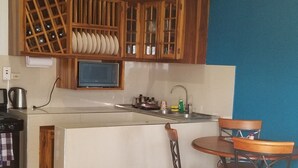 A compact kitchen with wooden cabinets, a microwave, and a sink. There is a dining area with a table and chairs, and a blue and white patterned rug on the floor. - This property is located near Public  and private beaches and restaurants.. (St Ann)