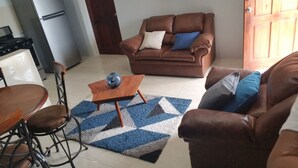 A living room with a brown leather sofa, a wooden coffee table, and a dining area with a table and chairs. - This property is located near Public  and private beaches and restaurants.. (St Ann)