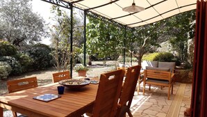 Une terrasse couverte avec une table en bois, des chaises et un canapé.