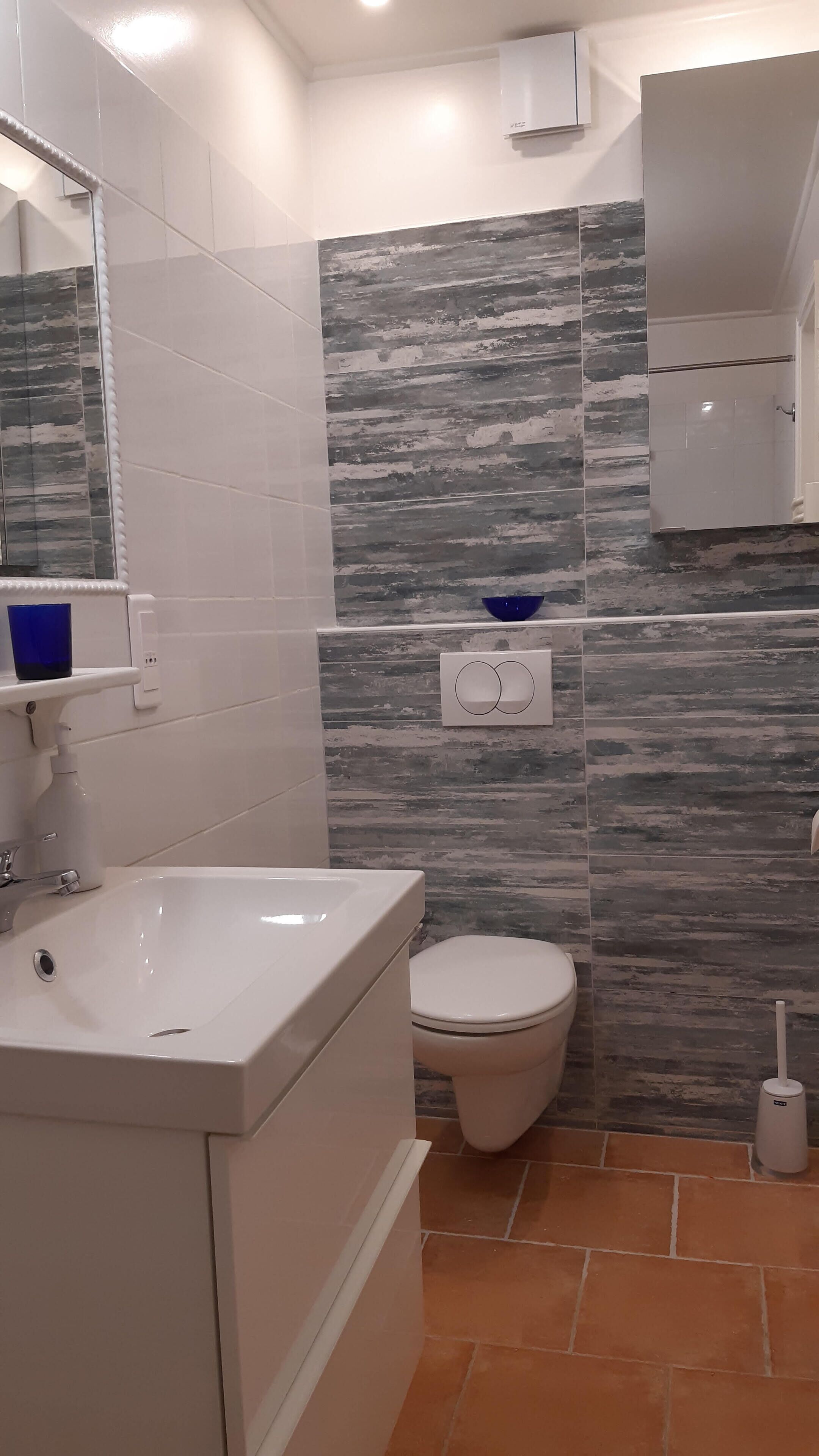 A bathroom with a white sink, a toilet, and a mirror. There is a blue bowl on the wall and a white cabinet above the toilet.