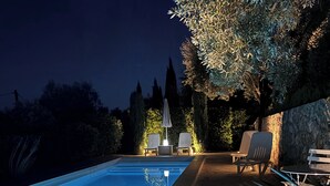 Une piscine extérieure dotée d’une terrasse carrelée en pierre, de deux chaises longues et d’une table avec un parasol.