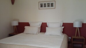 Un lit bien fait, avec du linge de lit blanc et des oreillers, deux tables de chevet avec des lampes et un tableau encadré au mur.