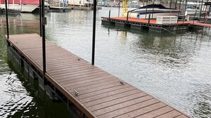 Un muelle de madera se extiende sobre aguas tranquilas, con barcos amarrados cerca y una zona cubierta en lo alto.