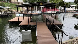 Un muelle con un área de descanso cubierta, un barco atracado al fondo y un edificio con toldo rojo.