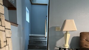 Una escalera de madera que conduce a un segundo piso, una pared de piedra, una lámpara sobre una pequeña mesa y un sofá marrón.