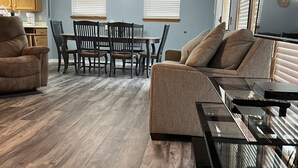 Una sala de estar con un sofá, una mesa de comedor con sillas y una cocina con armarios.