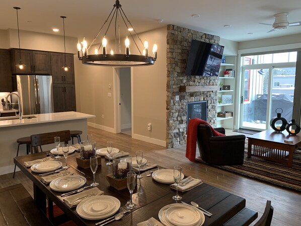 A modern kitchen with a stone accent wall, a dining area set for six, and a living space with a fireplace. - Stunning BRAND NEW Luxury condo in heart of downtown WP on the top floor (Winter Park)