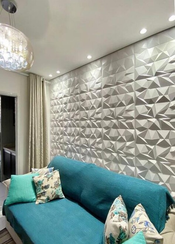 Una sala moderna con un sofá color turquesa, cojines estampados y un diseño geométrico en la pared.
