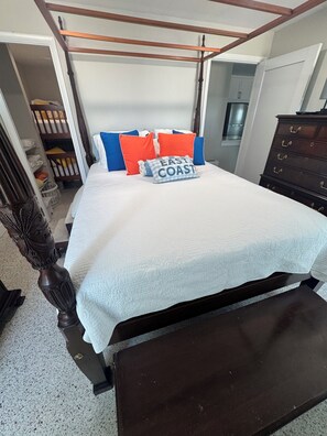 A four-poster bed with a white quilt and a pillow with 'EAST COAST' text, a wooden dresser, and a closet with folded clothes. - New Listing- Direct Oceanfront -Steps to the SAND -Cocoa Beach Getaway!! (Cocoa Beach)