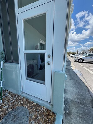 A white door with a glass panel, a small step leading to the entrance, and a gravel path.