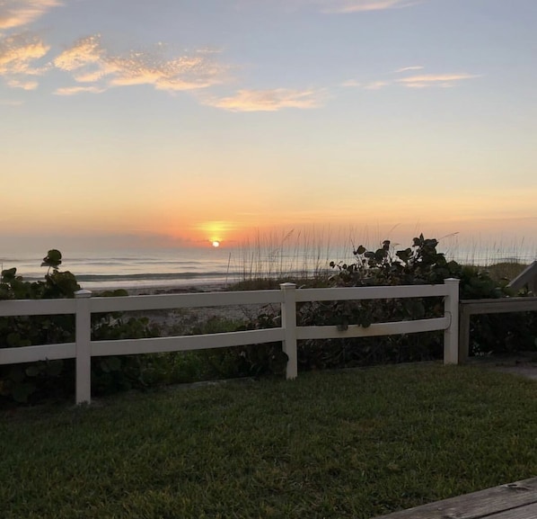 Vista do pôr do sol de uma área gramada com uma cerca branca ao primeiro plano.
