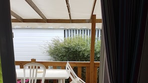 A wooden deck with a table and chairs, a view of the sea, and a curtain partially covering the entrance.