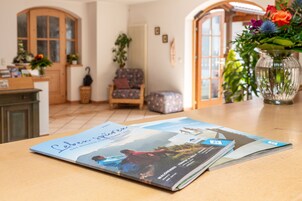 A magazine on a table in a room with a wooden floor, a chair, and a vase with flowers.