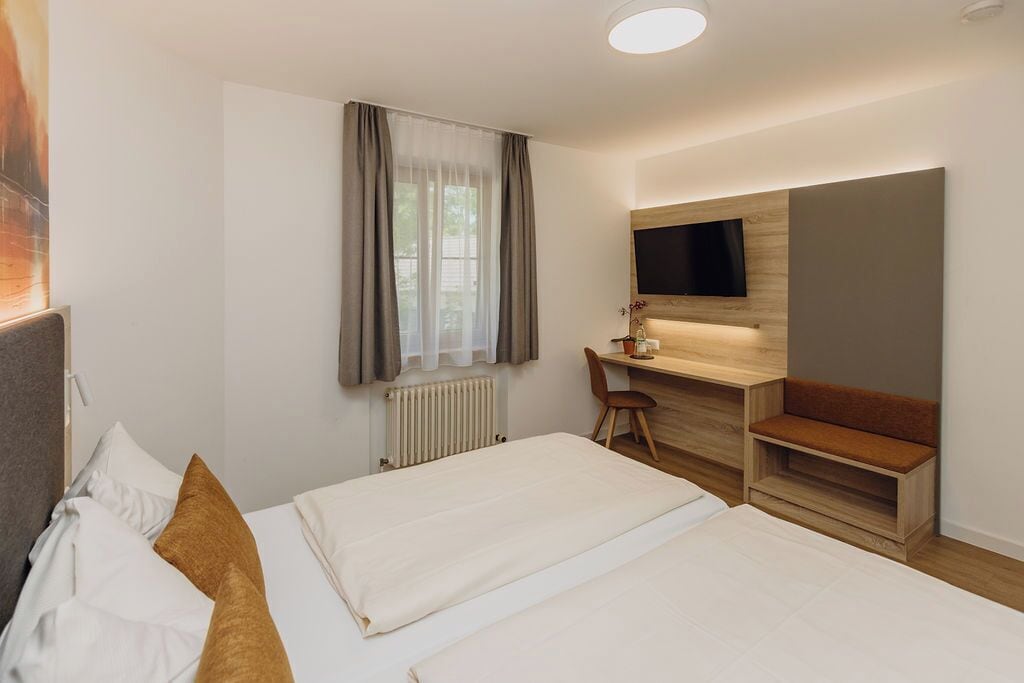 A hotel room with two beds, a desk, a chair, a TV, and a window with curtains.