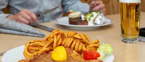 A plate of food with a fried cutlet, onion rings, and a lemon slice, accompanied by a glass of beer.