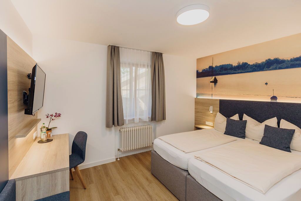 Habitación de hotel con cama, escritorio, silla, televisor y un cuadro en la pared.