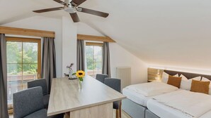 Une chambre moderne avec une table à manger, deux canapés gris, un ventilateur de plafond et un lit avec une literie blanche.