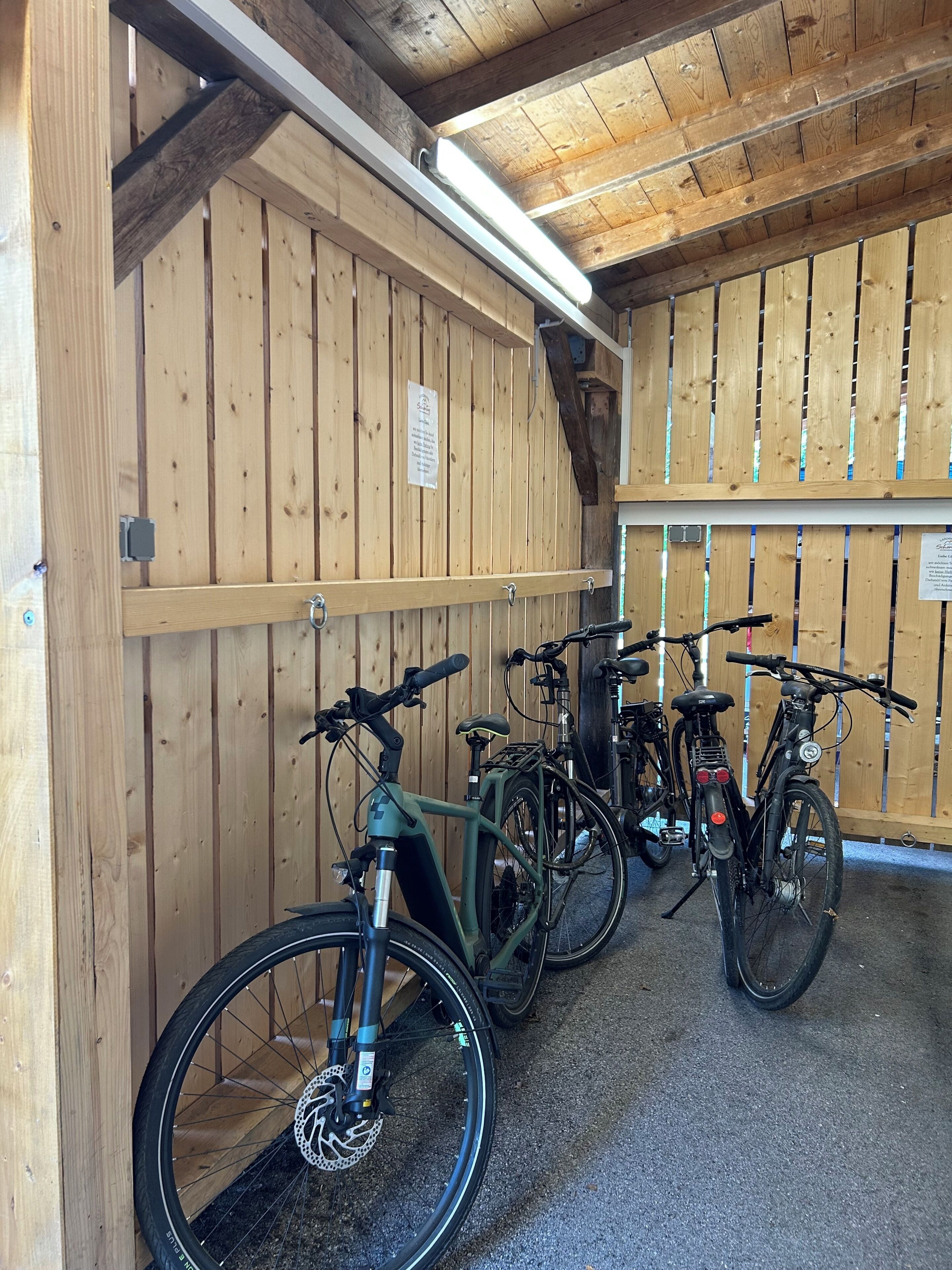 Interior de madera con bicicletas apoyadas en la pared, una lámpara en el techo y un cartel en la pared.