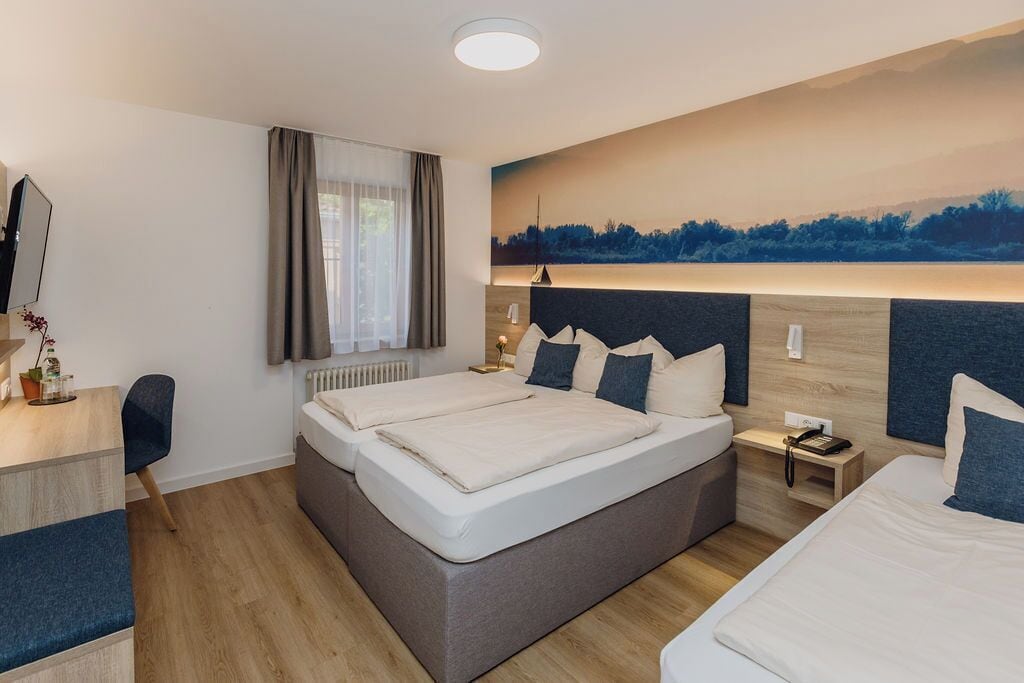A modern hotel room with a large bed, a desk, and a painting of a landscape on the wall.