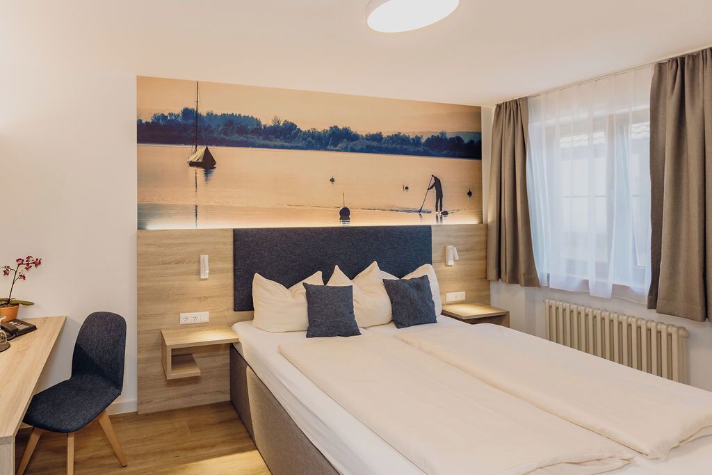 Una habitación de hotel moderna con una cama grande, un escritorio y un cuadro de un paisaje lacustre.