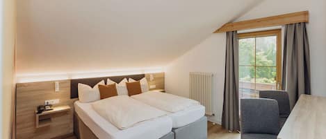 A bedroom with a bed, bedside table, chair, and a window with curtains.