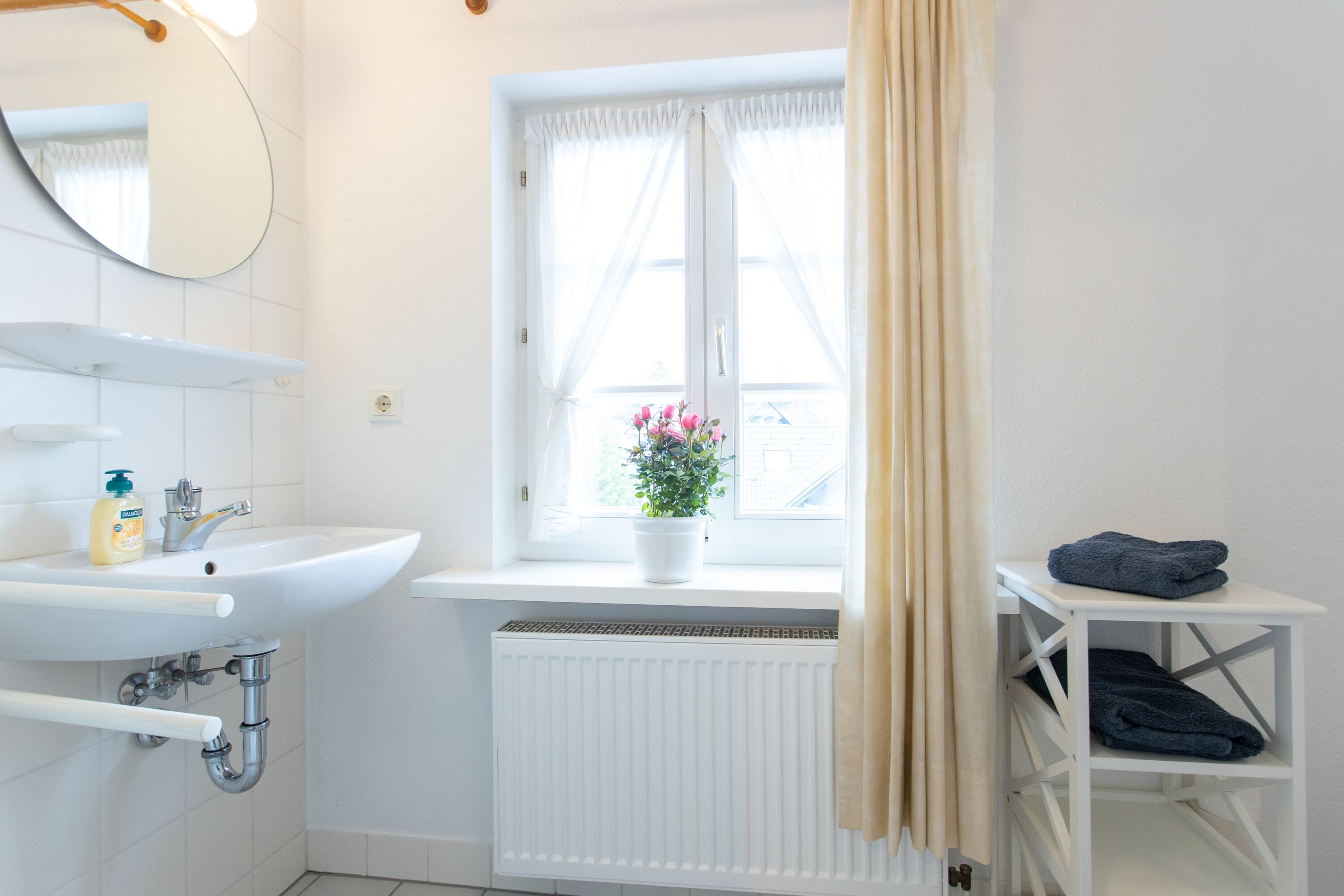 Une salle de bain avec un lavabo blanc, un miroir et une fenêtre avec des rideaux.