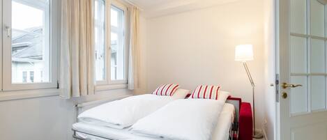 Una habitación de hotel con una cama, una lámpara de noche, una ventana con cortinas y una puerta.