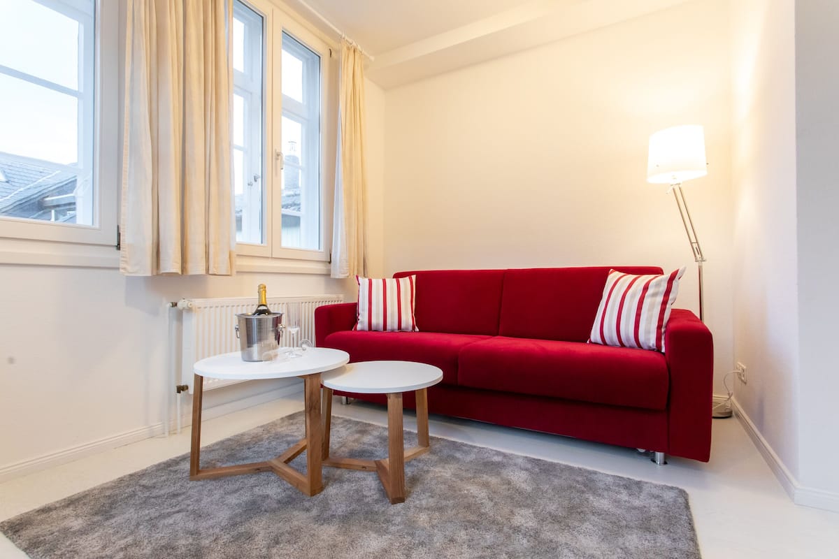 A red sofa with striped pillows, a white table with a metal container, and a grey carpet.