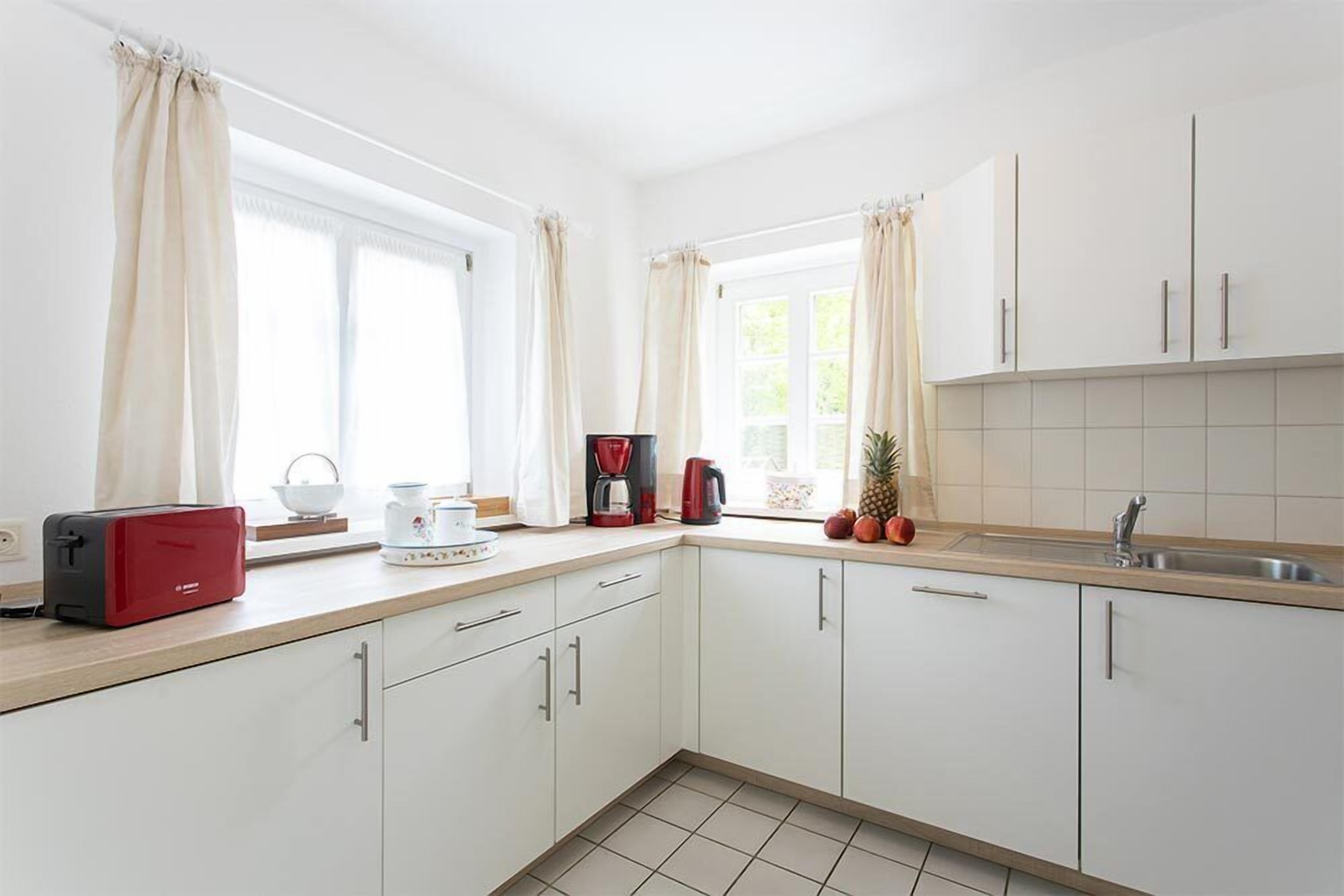 A modern kitchen with white cabinets, a red toaster, a coffee maker, and a window with curtains.