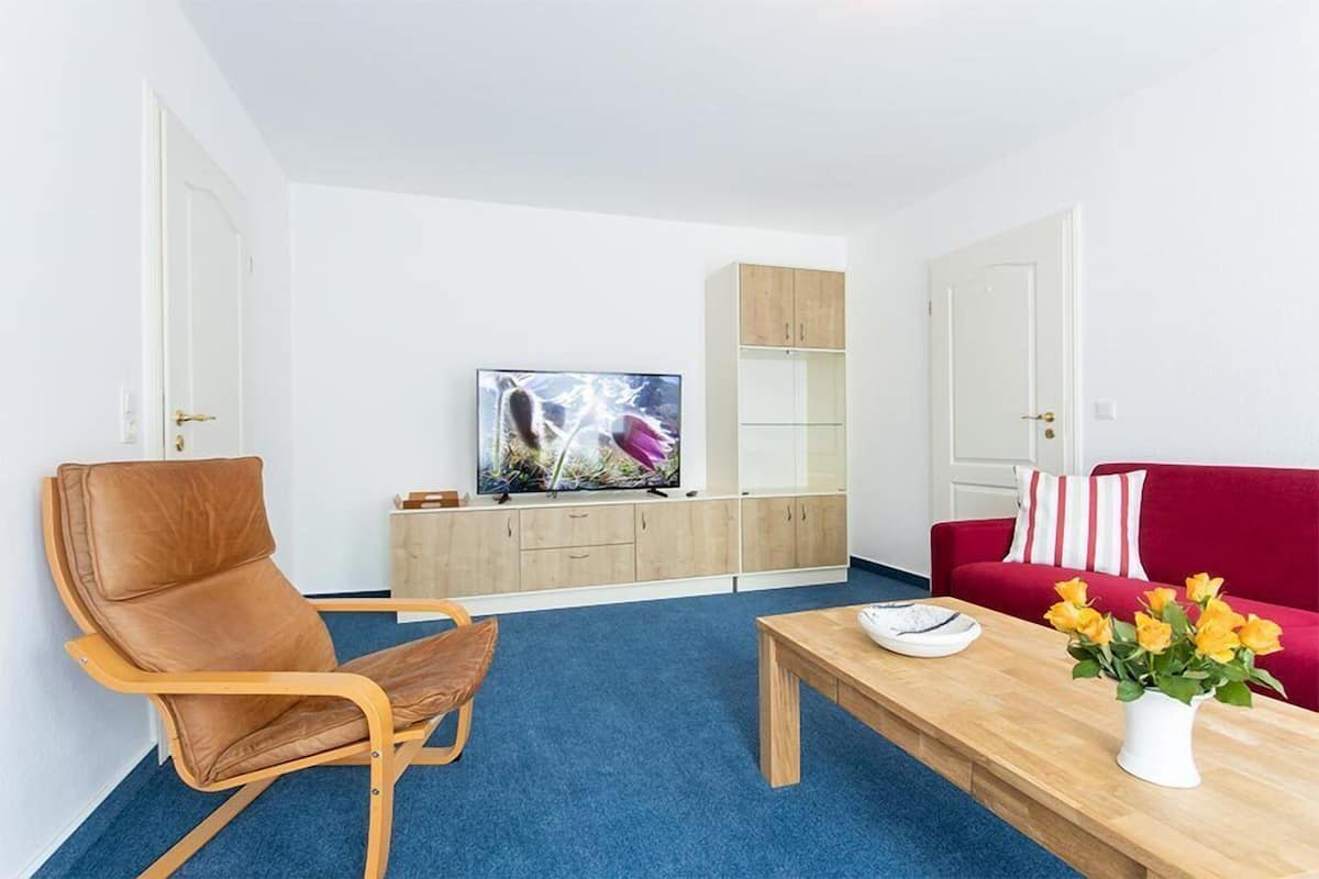 A modern living room with a brown leather chair, a red sofa, a wooden coffee table, and a TV on a white cabinet.
