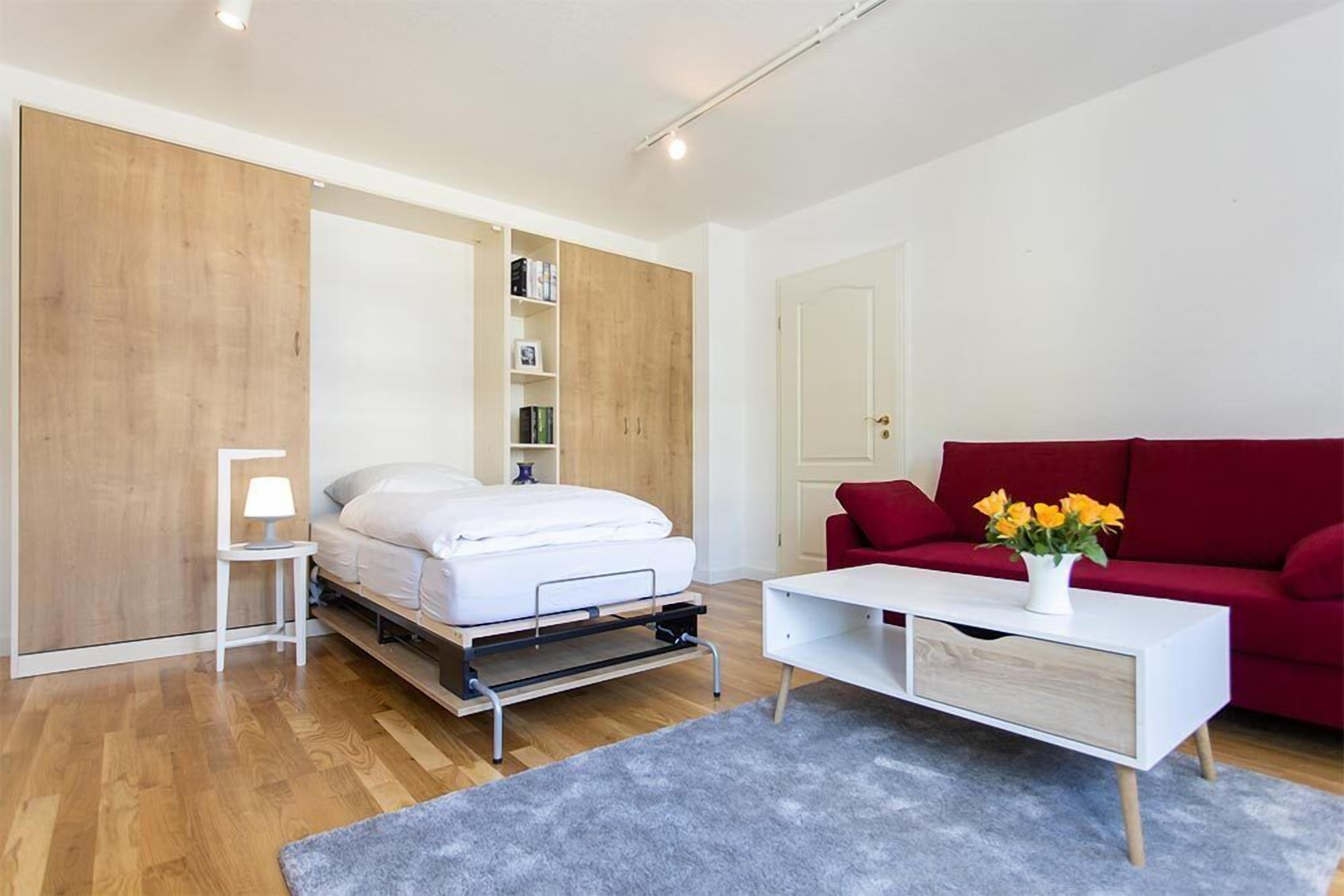 A modern room with a bed, a red sofa, a white side table, and a small white cabinet.