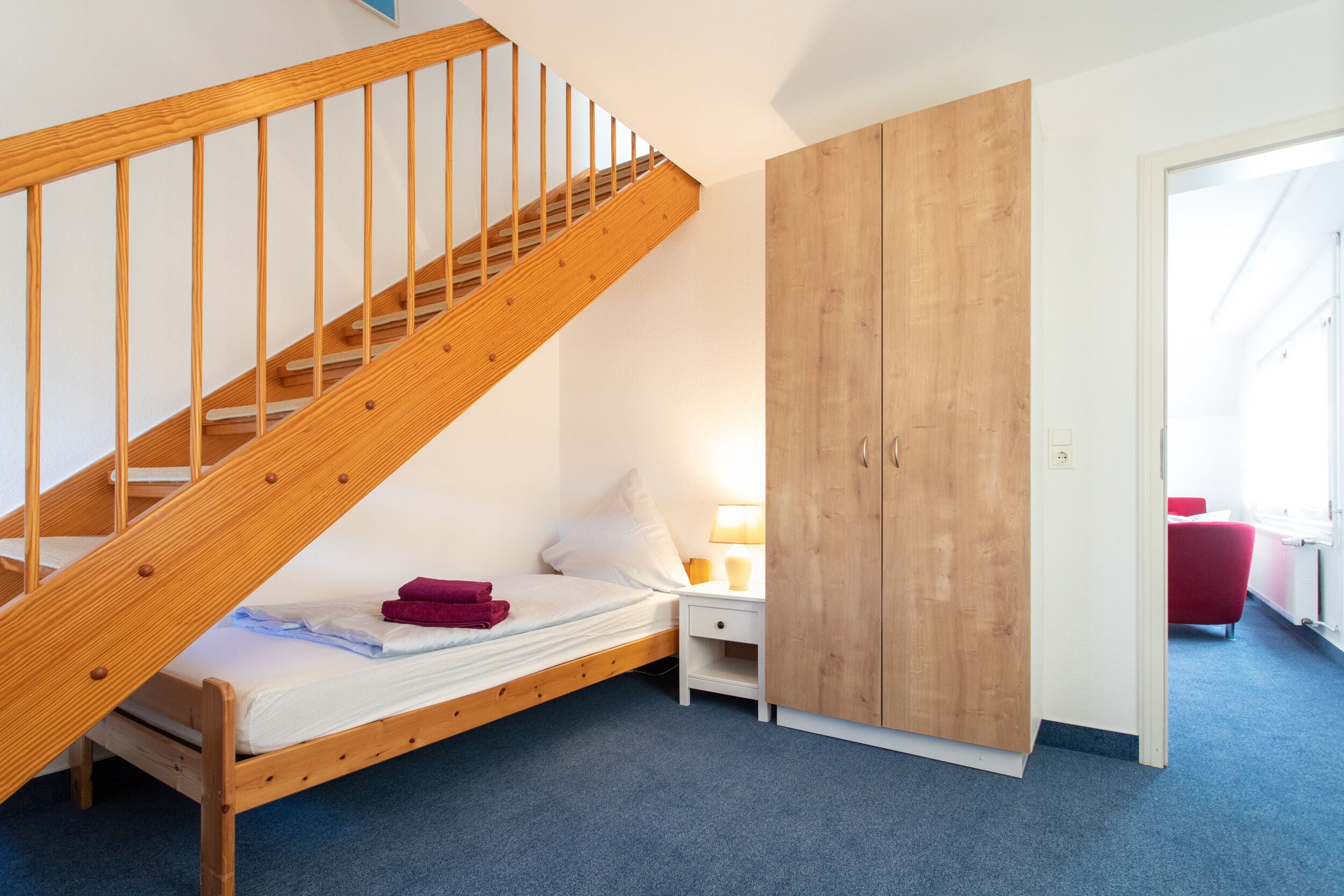 A bedroom with a wooden staircase, a single bed, a nightstand with a lamp, and a wardrobe.