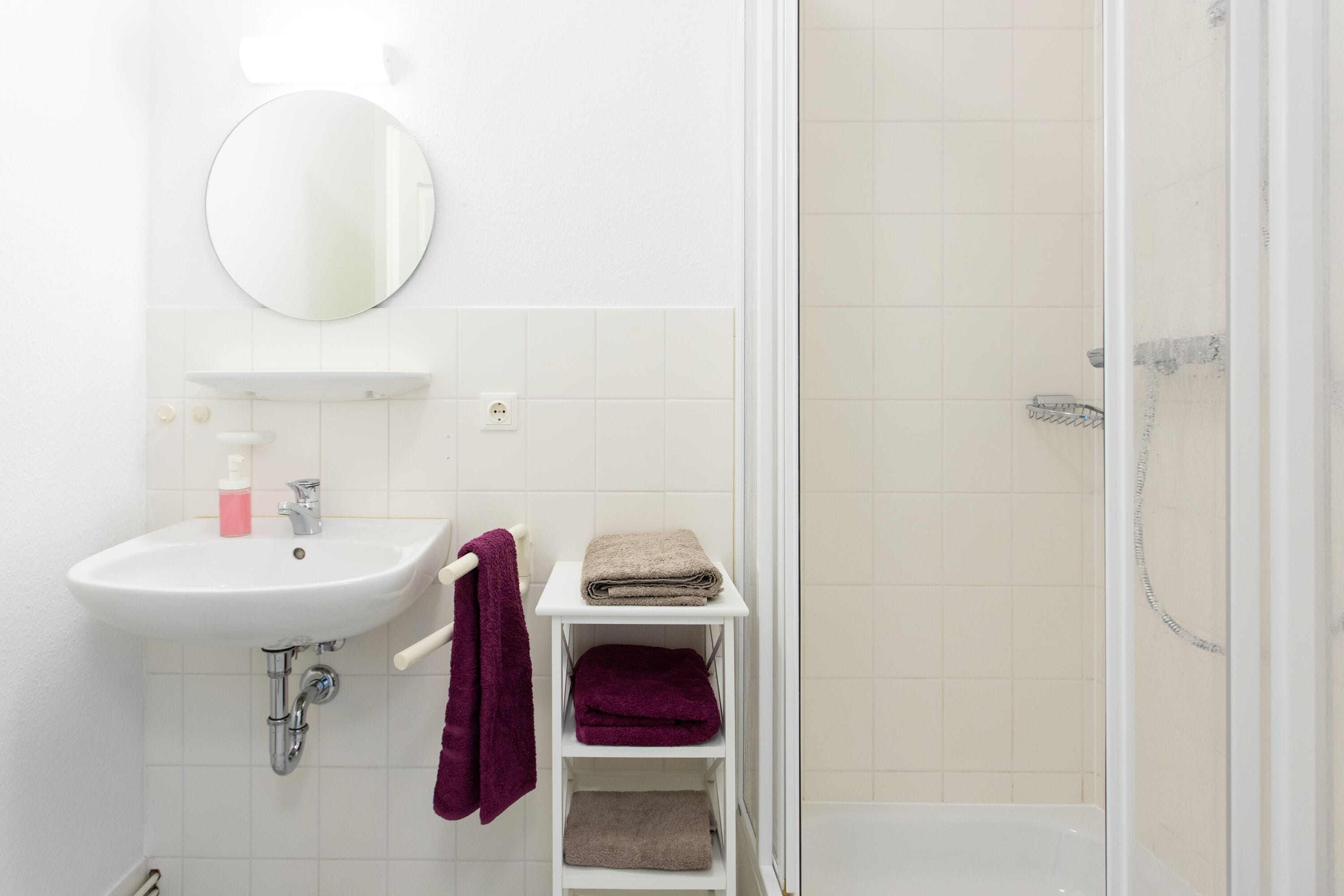 Een badkamer met een wit wastafelmeubel, spiegel en douche.