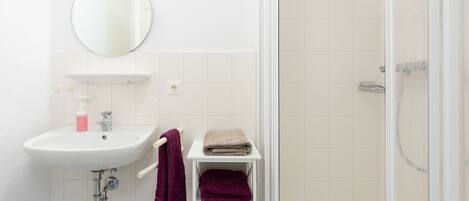Een badkamer met een wit wastafelmeubel, spiegel en douche.
