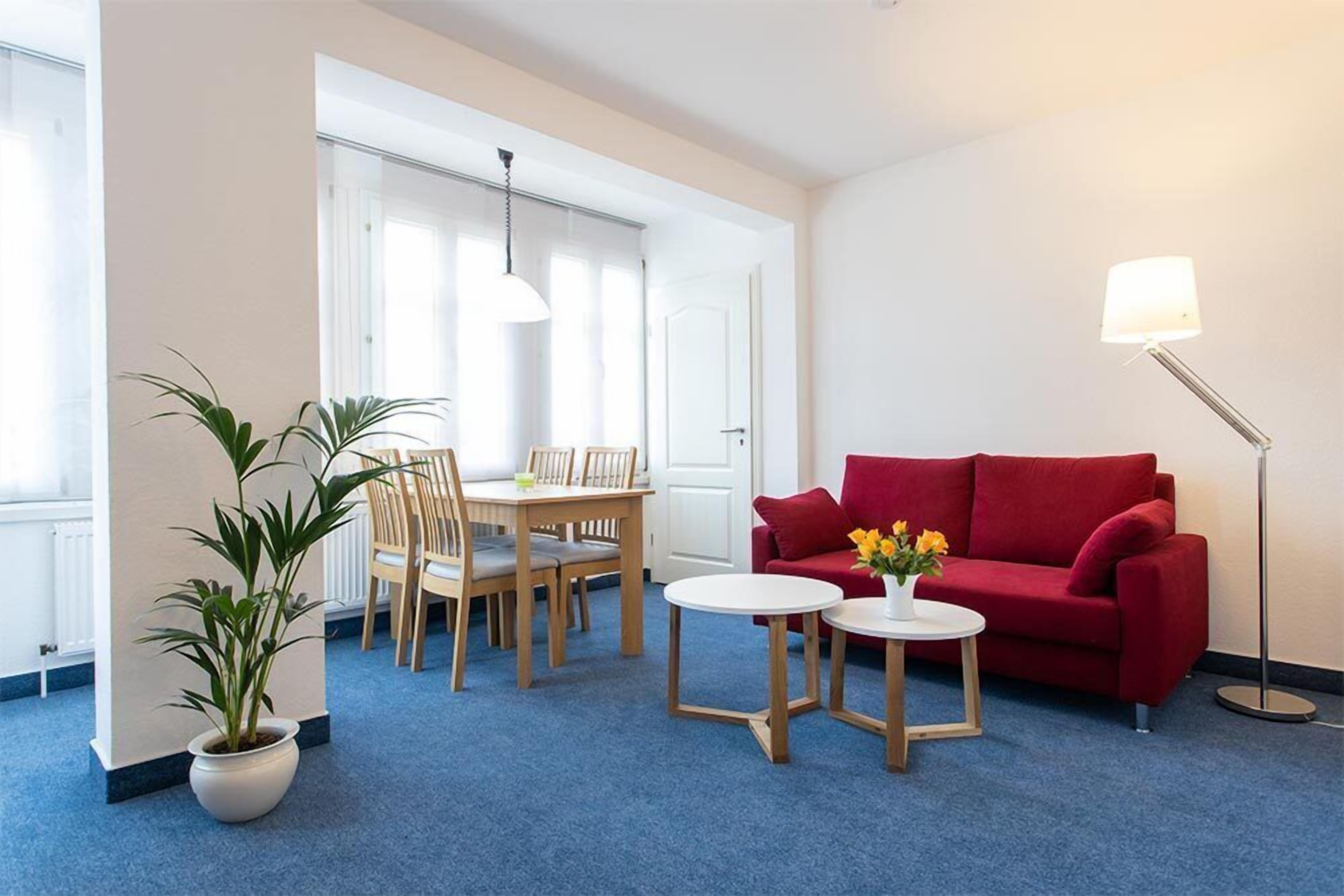 Un salon moderne avec un canapé rouge, une table basse ronde, une plante en pot, une table à manger avec des chaises et un lampadaire.